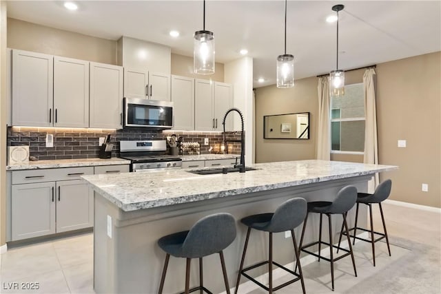 kitchen featuring stainless steel appliances, decorative light fixtures, a kitchen island with sink, and sink