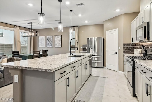 kitchen featuring sink, appliances with stainless steel finishes, hanging light fixtures, light stone counters, and an island with sink