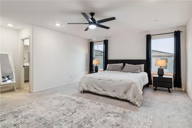 carpeted bedroom featuring ceiling fan, ensuite bathroom, and multiple windows