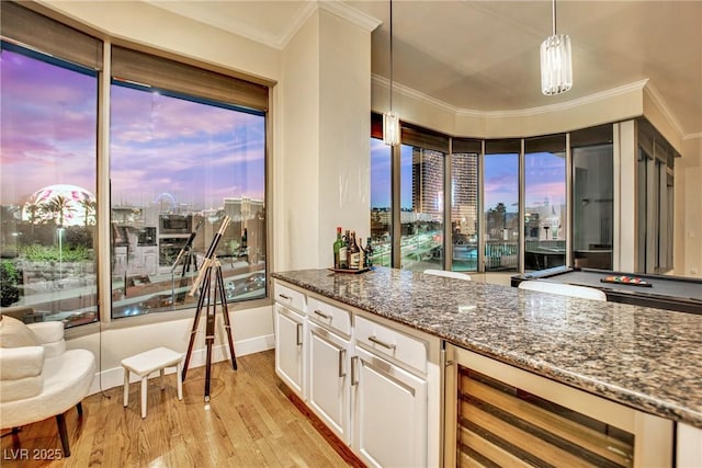 bar featuring dark stone countertops, white cabinets, hanging light fixtures, ornamental molding, and light hardwood / wood-style floors