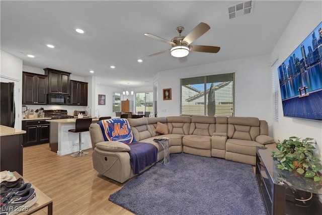 living room with ceiling fan with notable chandelier and light wood-type flooring