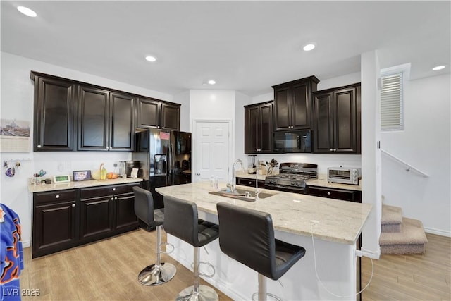 kitchen with a breakfast bar, an island with sink, sink, black appliances, and light hardwood / wood-style flooring