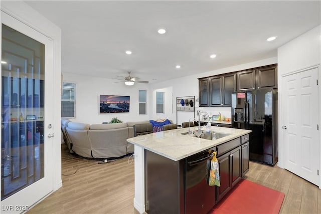 kitchen featuring sink, light hardwood / wood-style flooring, dark brown cabinets, black appliances, and a center island with sink