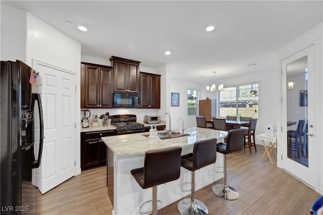 kitchen with a center island with sink, a breakfast bar area, hanging light fixtures, and black appliances