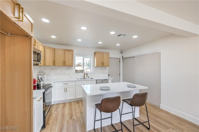 kitchen with stainless steel appliances, a sink, light countertops, a center island, and a kitchen bar