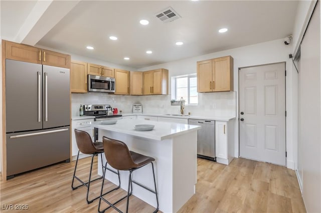 kitchen featuring visible vents, a breakfast bar area, a center island, stainless steel appliances, and light countertops