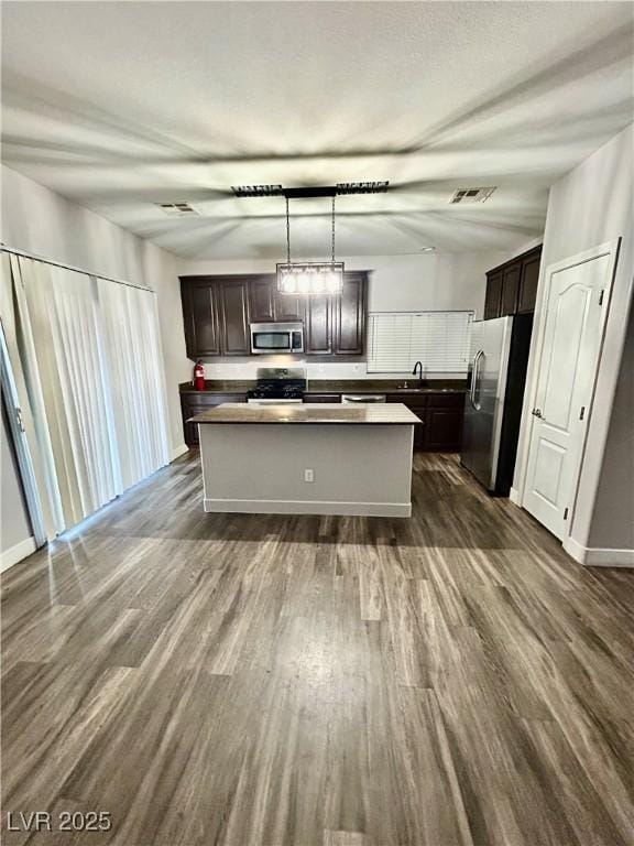 kitchen featuring dark wood-type flooring, a kitchen island, stainless steel appliances, and decorative light fixtures