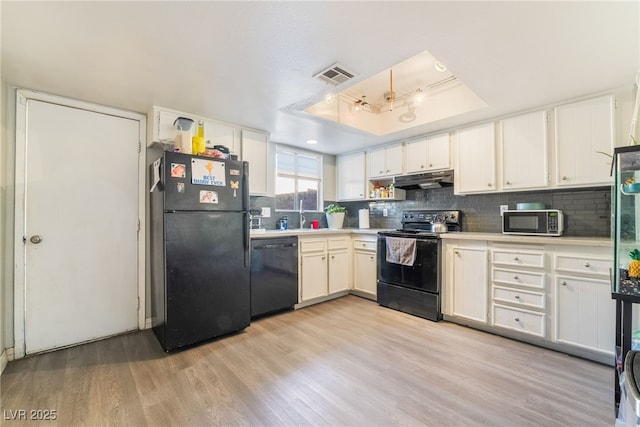 kitchen featuring a raised ceiling, backsplash, light wood-type flooring, and black appliances