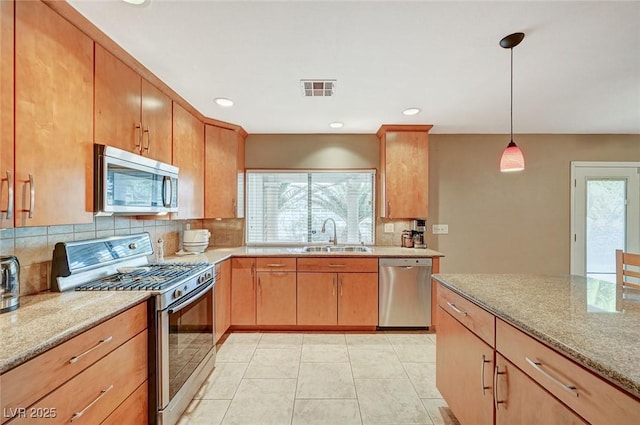 kitchen featuring sink, stainless steel appliances, light stone counters, and decorative light fixtures