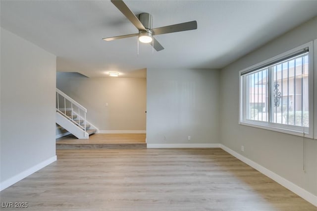 unfurnished room with ceiling fan, stairway, light wood-style flooring, and baseboards