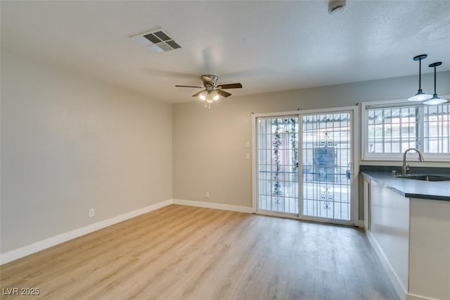 interior space with light wood finished floors, baseboards, visible vents, and a sink