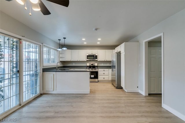 kitchen featuring a sink, white cabinets, hanging light fixtures, appliances with stainless steel finishes, and dark countertops