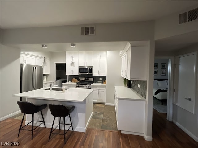 kitchen with appliances with stainless steel finishes, pendant lighting, white cabinetry, decorative backsplash, and a kitchen island with sink