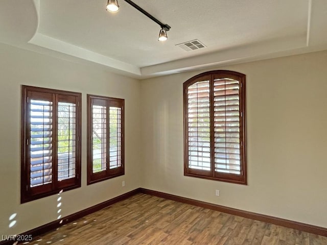 spare room featuring wood-type flooring, a tray ceiling, and rail lighting