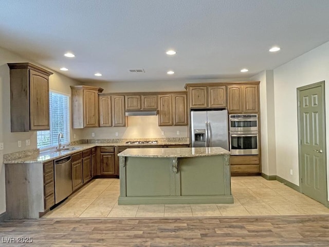 kitchen featuring sink, light stone countertops, a center island, and appliances with stainless steel finishes