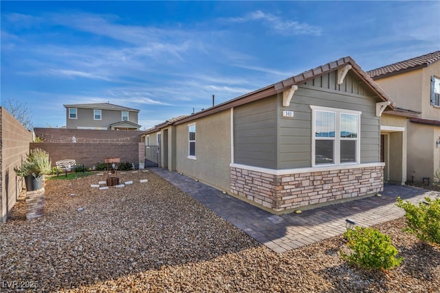 view of home's exterior with stone siding, a patio area, and a fenced backyard