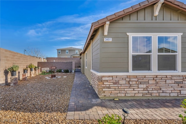 view of side of property featuring stone siding, a fenced backyard, a patio area, and board and batten siding