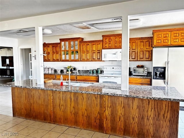 kitchen with white appliances, dark stone counters, sink, and light tile patterned floors