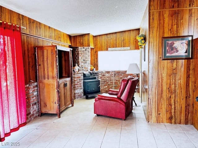 living area with light tile patterned floors, a textured ceiling, a wood stove, and wood walls