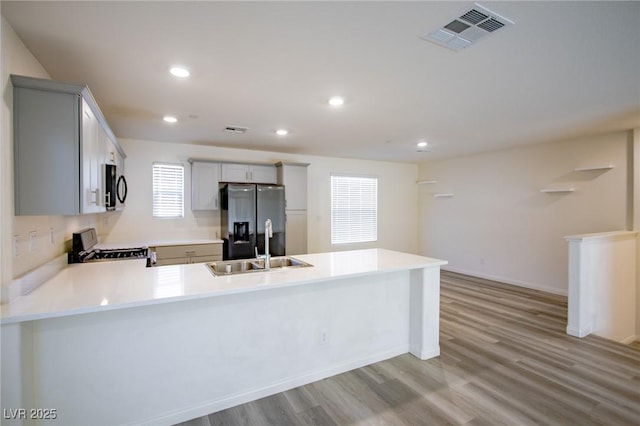 kitchen with range with gas cooktop, sink, kitchen peninsula, stainless steel refrigerator with ice dispenser, and light wood-type flooring