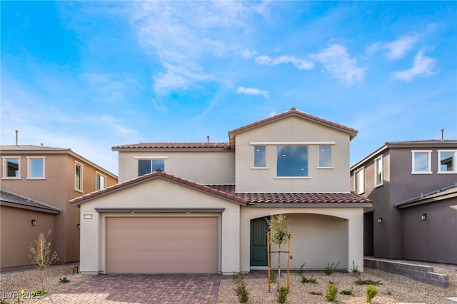 mediterranean / spanish-style house with stucco siding, a tiled roof, an attached garage, and decorative driveway