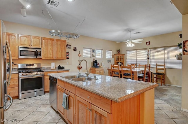 kitchen with appliances with stainless steel finishes, an island with sink, sink, light tile patterned floors, and light stone countertops