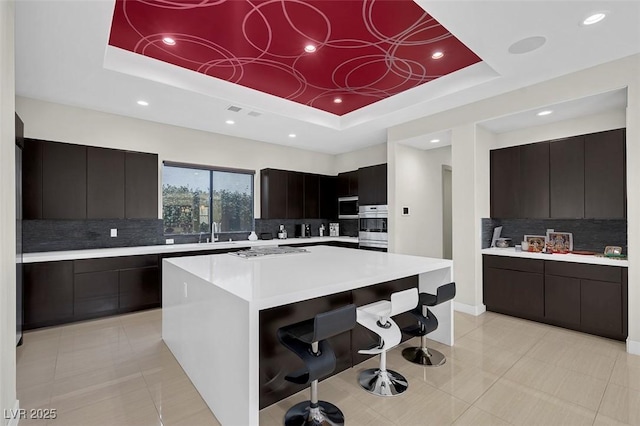 kitchen featuring sink, tasteful backsplash, a center island, appliances with stainless steel finishes, and a raised ceiling