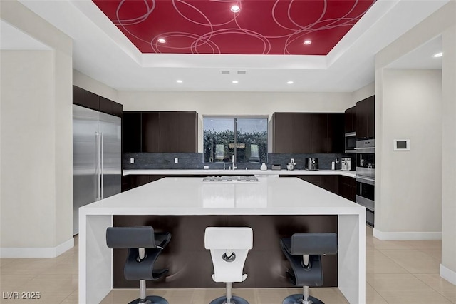 kitchen featuring stainless steel appliances, a kitchen island, a breakfast bar, and a tray ceiling