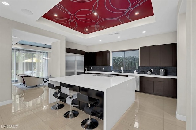 kitchen with sink, appliances with stainless steel finishes, a kitchen island, decorative backsplash, and a raised ceiling