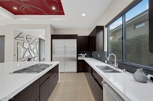 kitchen featuring sink, dark brown cabinets, a tray ceiling, stainless steel appliances, and backsplash