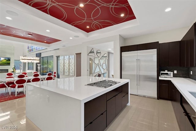 kitchen with appliances with stainless steel finishes, tasteful backsplash, a tray ceiling, a kitchen island, and light tile patterned flooring