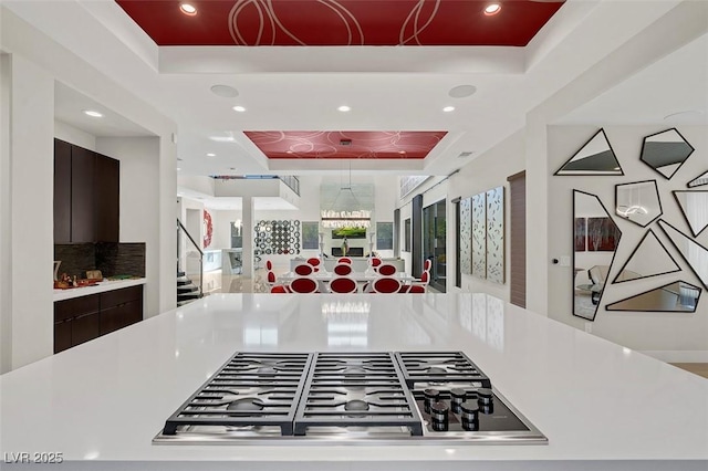 kitchen featuring decorative backsplash, dark brown cabinets, a raised ceiling, and stainless steel gas stovetop