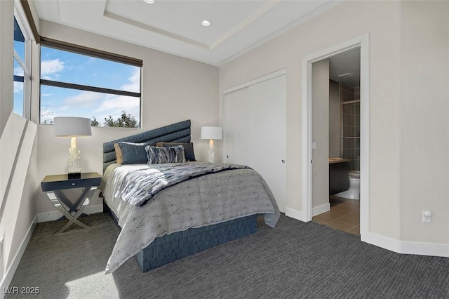 carpeted bedroom featuring a raised ceiling and ensuite bathroom