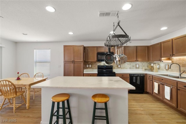 3924 E Garfield Dr, Pahrump, NV 89061 - kitchen featuring visible vents, a breakfast bar, light wood-style floors, black appliances, and a sink