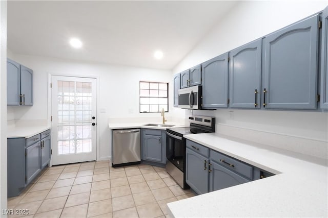 kitchen with blue cabinetry, light tile patterned flooring, lofted ceiling, sink, and appliances with stainless steel finishes