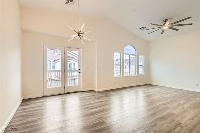 empty room with ceiling fan with notable chandelier, plenty of natural light, vaulted ceiling, and wood-type flooring