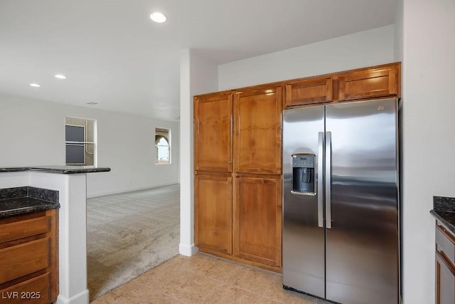 kitchen featuring dark stone countertops, stainless steel fridge, and light colored carpet