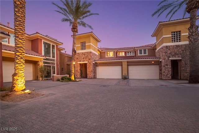 view of front of property with stone siding, an attached garage, driveway, and stucco siding