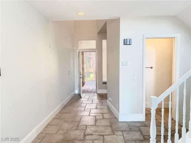 corridor with stone tile floors, stairs, and baseboards