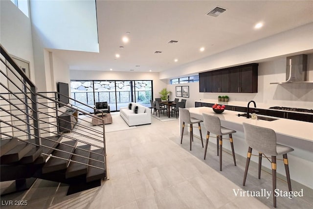 kitchen with visible vents, a kitchen breakfast bar, wall chimney range hood, a sink, and recessed lighting