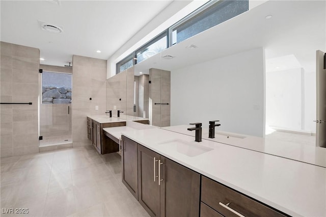 bathroom with a stall shower, tile patterned flooring, two vanities, and a sink