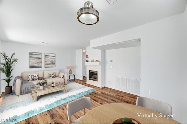 living area with a tiled fireplace, visible vents, and wood finished floors