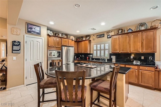 kitchen featuring sink, tasteful backsplash, a center island, light tile patterned floors, and appliances with stainless steel finishes