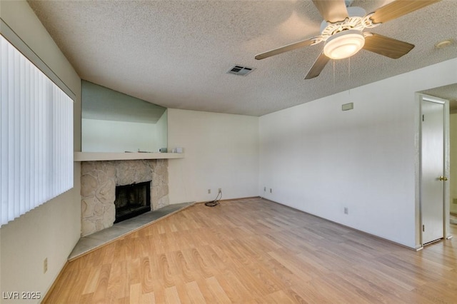 unfurnished living room featuring ceiling fan, a textured ceiling, a fireplace, and light wood-type flooring