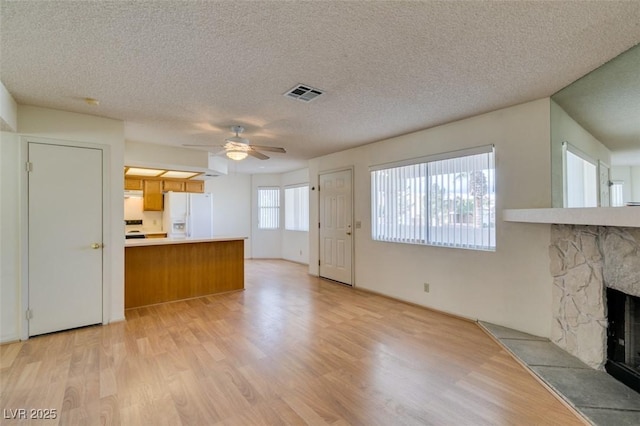 kitchen featuring a stone fireplace, white fridge with ice dispenser, ceiling fan, kitchen peninsula, and light wood-type flooring