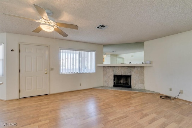 unfurnished living room with ceiling fan, a fireplace, a textured ceiling, and light wood-type flooring