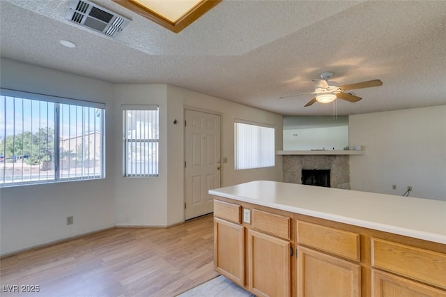 kitchen with a fireplace, light brown cabinetry, ceiling fan, a textured ceiling, and light wood-type flooring