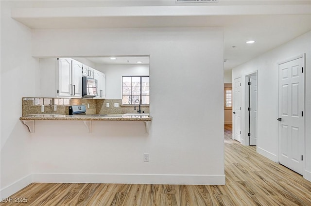 kitchen with electric stove, sink, a breakfast bar, white cabinets, and kitchen peninsula