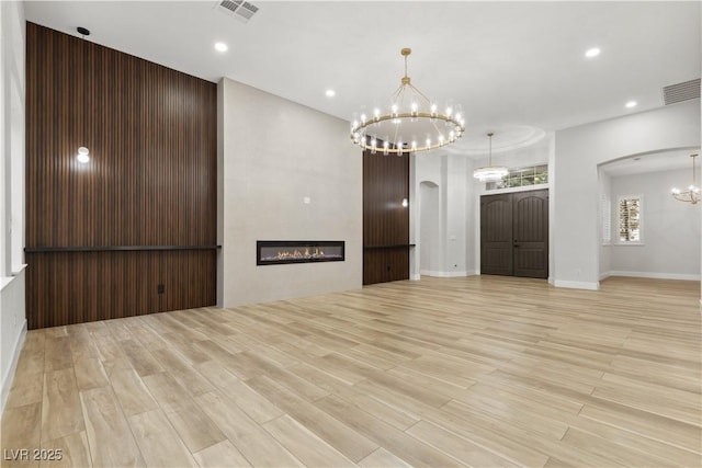 unfurnished room with light hardwood / wood-style floors, a chandelier, and a large fireplace