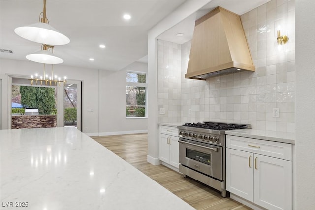 kitchen with white cabinetry, custom range hood, stainless steel range, and decorative light fixtures